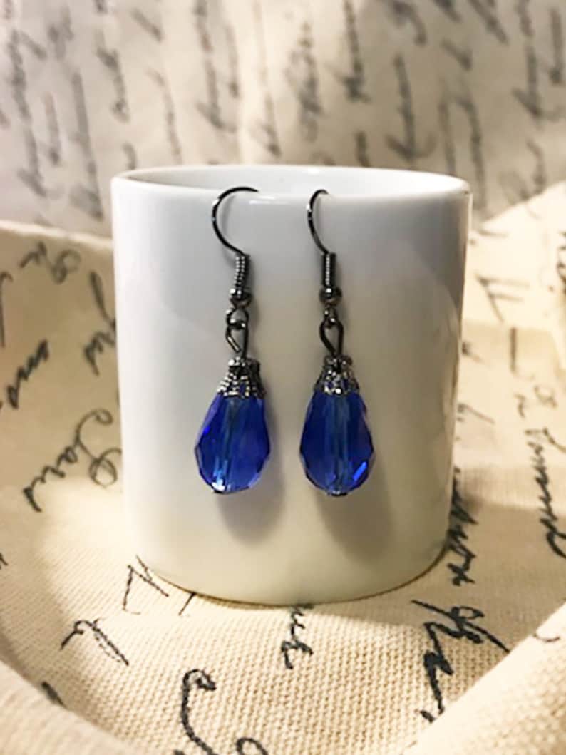 May include: A pair of dangle earrings with blue crystal teardrop shaped stones and silver-toned metal accents.