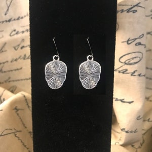 May include: A pair of silver earrings with a textured, circular design. The earrings are hanging from a black velvet background.
