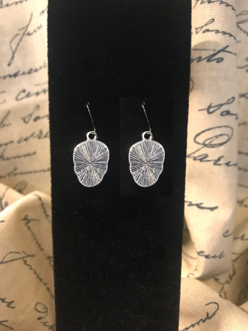 May include: A pair of silver earrings with a textured, circular design. The earrings are hanging from a black velvet background.