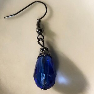 May include: A single blue teardrop-shaped crystal earring with a silver filigree setting and a silver hook.