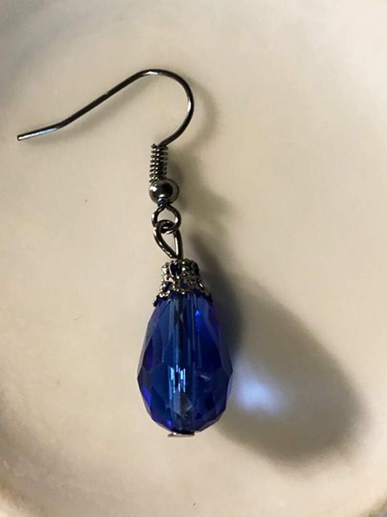 May include: A single blue teardrop-shaped crystal earring with a silver filigree setting and a silver hook.