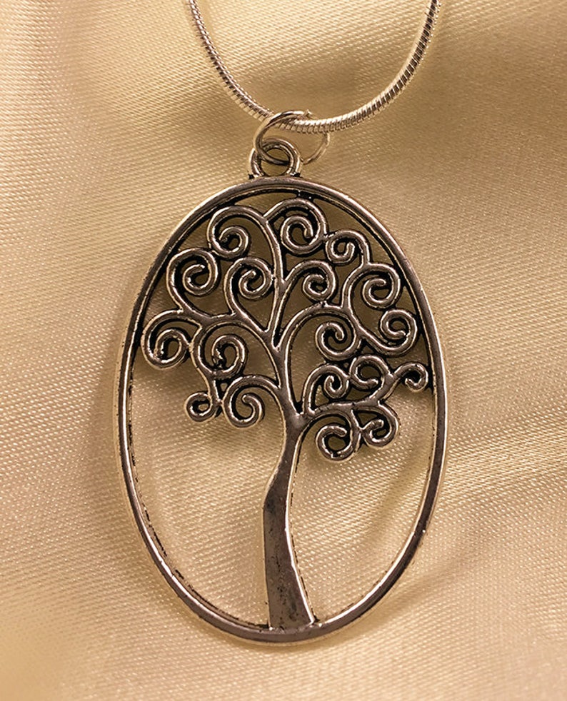 May include: A silver necklace with a pendant shaped like a tree with a swirling design. The pendant is oval shaped and hangs from a silver chain.