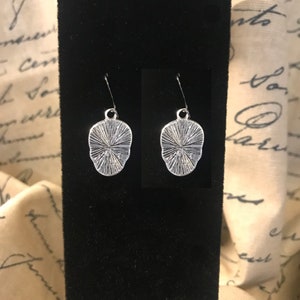 May include: A pair of silver earrings with a textured, circular design. The earrings are hanging from a black display card.