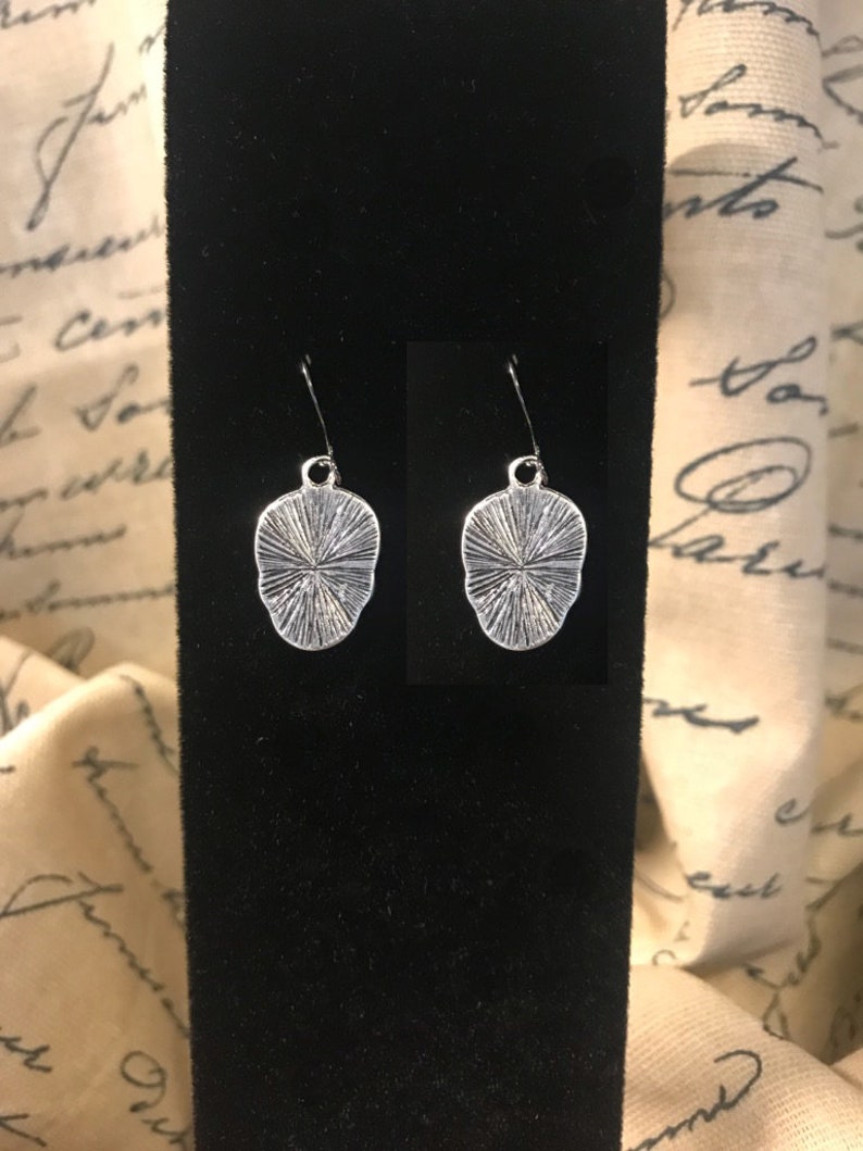May include: A pair of silver earrings with a textured, circular design. The earrings are hanging from a black display card.