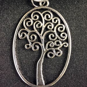 May include: A silver oval pendant necklace featuring a tree of life design with intricate swirls and branches.