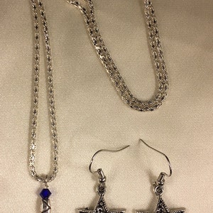 May include: A silver chain necklace with a blue crystal and a silver Star of David pendant. Matching silver Star of David earrings with blue crystals.