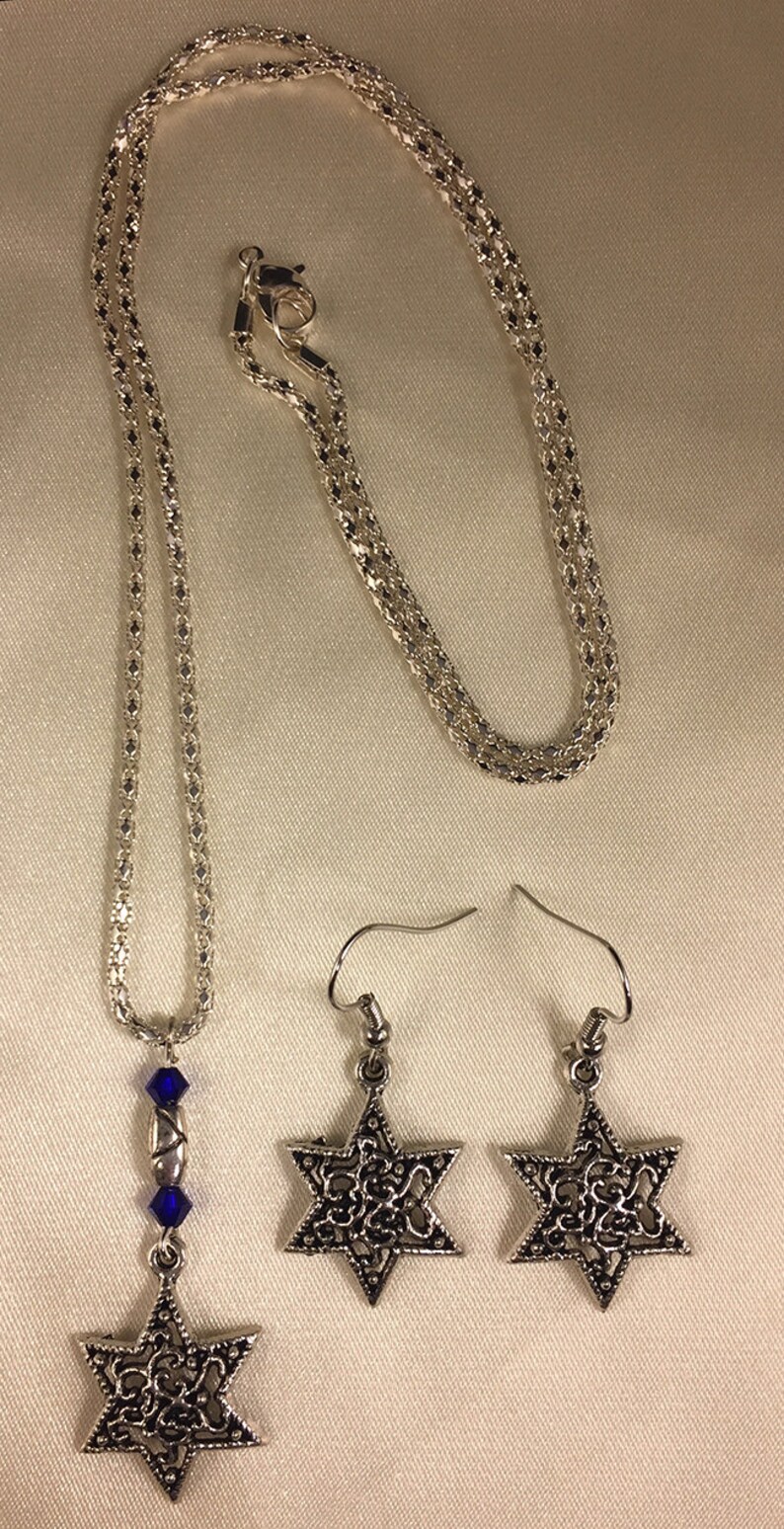 May include: A silver chain necklace with a blue crystal and a silver Star of David pendant. Matching silver Star of David earrings with blue crystals.