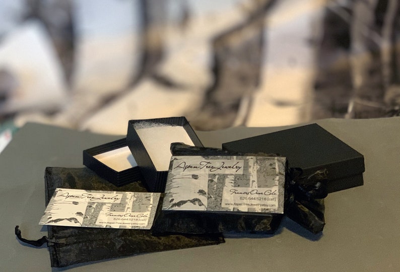 May include: A black velvet pouch with a white business card that reads "Aspen Tree Jewelry" and "Frances Owen Cole". The pouch is next to a black box with a white interior and a second black box with a white interior.