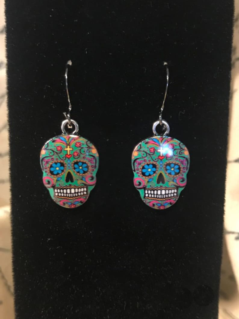 May include: A pair of silver dangle earrings with a green, blue, pink, and gold sugar skull design.