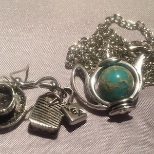 May include: A silver teapot necklace with a turquoise gemstone, a silver teacup earring, and a silver tea bag charm. The necklace has a silver chain.