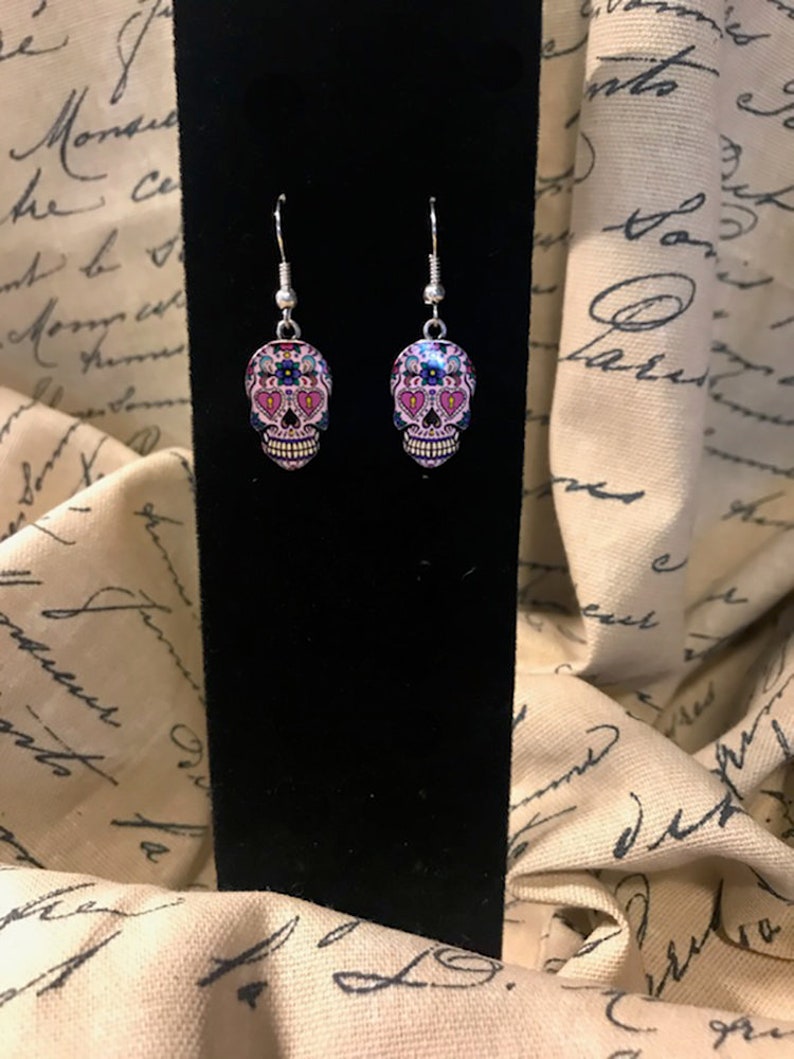 May include: A pair of silver dangle earrings with pink, blue, and black sugar skull charms.