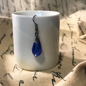 May include: A single blue teardrop-shaped glass earring with a silver-toned metal setting and a hook closure.