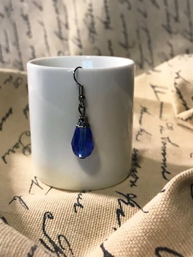 May include: A single blue teardrop-shaped glass earring with a silver-toned metal setting and a hook closure.
