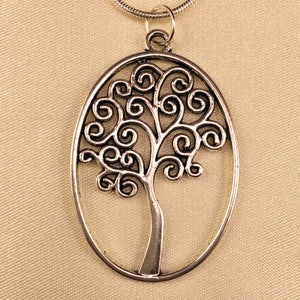 May include: A silver oval pendant necklace featuring a tree of life design with intricate swirls and branches.