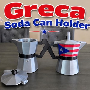 May include: Two silver soda can holders, one with a Puerto Rican flag design, and the other plain. The holders are shaped like coffee makers and are on a wooden table. The text "Greca Soda Can Holder" is displayed above the holders.
