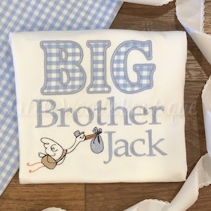 May include: White onesie with blue gingham print letters spelling "BIG BROTHER JACK" and a blue gingham stork carrying a baby in a blue bag.