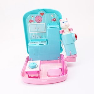 May include: A pink and blue toy playset featuring a white cat figure. The playset opens to reveal a kitchen and bathroom interior with a stove, sink, and toilet.