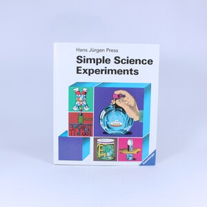 May include: A book titled "Simple Science Experiments" by Hans Jürgen Press. The cover features colourful illustrations of science experiments, including a bottle with a ship inside, a jar with a plant, and a device with a spinning wheel.