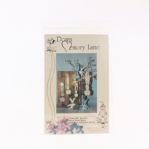 May include: A package with the text "Down Emory Lane" and a drawing of bunnies hanging on a tree. The text "Hang Me Bunnies, Door-Knob Bunny, Easter or Christmas Bunny" is also visible. Pink and blue ribbon accents the bottom of the package.