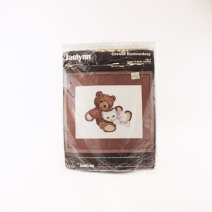 May include: A brown and white crewel embroidery kit featuring a brown teddy bear hugging a white kitten. The kit is packaged in a clear plastic bag with the text "Janlynn Crewel Embroidery 426-B Teddy's Best Friend".