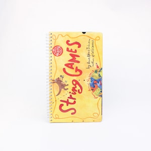May include: A yellow book titled "String Games" by Anne Akers Johnson, author of "Cat's Cradle". The book features a colourful world map and a kangaroo illustration.