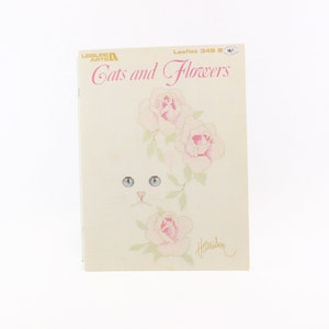 May include: A cross-stitch pattern booklet featuring a white cat's face and pink roses. The title is "Cats and Flowers" and the leaflet number is 349.