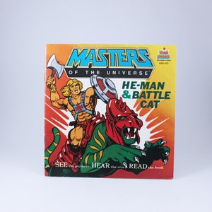May include: A vintage Masters of the Universe book featuring He-Man and Battle Cat. The cover is orange and yellow with a cartoon illustration of He-Man riding Battle Cat. The text on the cover reads "Masters of the Universe", "He-Man & Battle Cat", "See the pictures Hear the story Read the book", and "KSR 613".