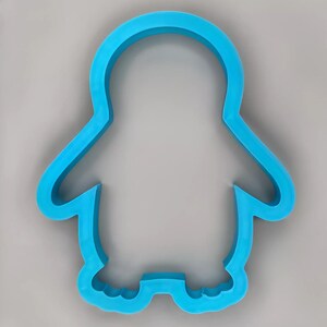 May include: A blue plastic penguin cookie cutter. The cutter is shaped like a penguin with a rounded body, small wings, and a flat bottom.