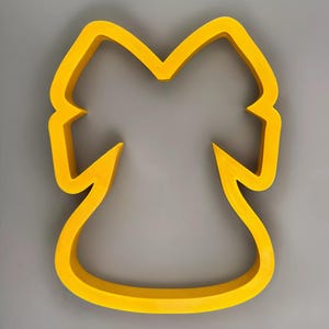 May include: A bright yellow cookie cutter in the shape of a bow. The cutter has a rounded bottom and a detailed top, with a smooth, clean finish. The cutter is set against a gray background.