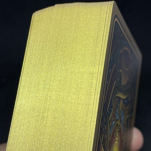 May include: A deck of playing cards with a gold foil finish. The cards are stacked neatly and the edges are visible.