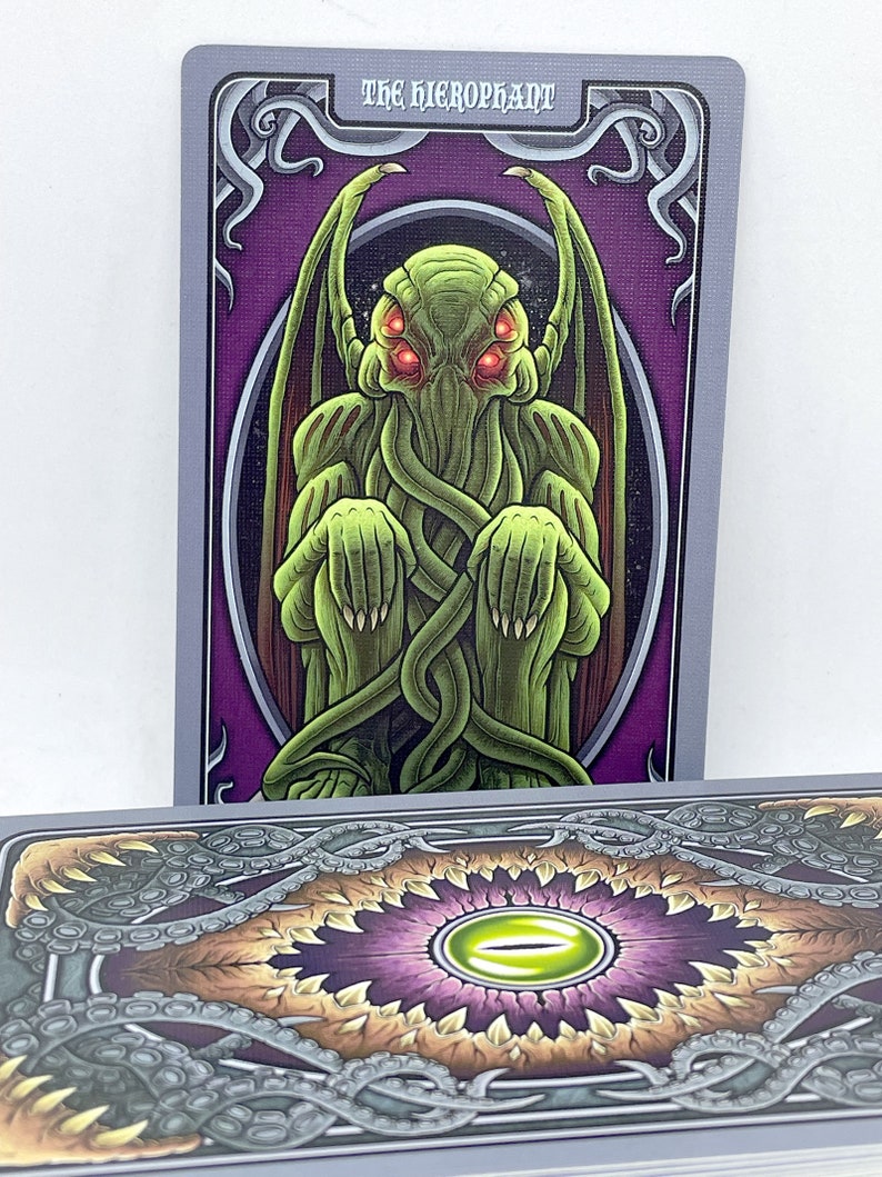 May include: Tarot card featuring a green, tentacled creature with red eyes, titled "The Hierophant". The card has a purple background with ornate gold trim.