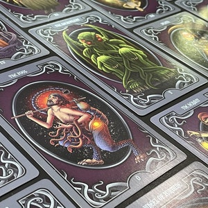 May include: A set of tarot cards with illustrations of various creatures and characters. The cards are purple with silver accents and feature ornate borders. The cards are numbered and have titles such as "The Fool" and "The Magician".