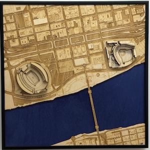 May include: A wooden 3D model of a city skyline with two stadiums, one for baseball and one for football, and a river running through it. The model is framed in black and has a blue background.