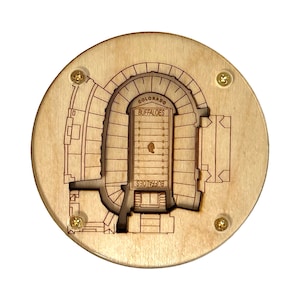 May include: A wooden coaster featuring a detailed laser-engraved design of Folsom Field, home of the University of Colorado Buffaloes football team. The coaster is circular and has a light brown wood finish.