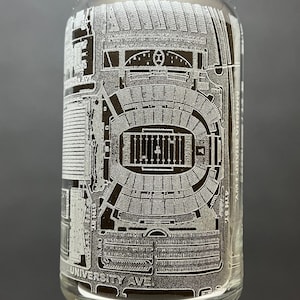 May include: A clear glass can with an etched design of a football stadium. The stadium is labeled "University Ave." and "4th St."
