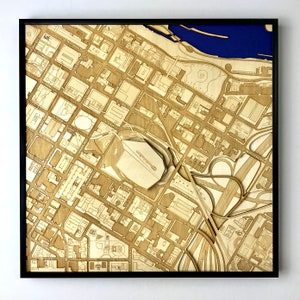 May include: A detailed laser-cut wooden map of a city, featuring a large stadium in the center. The map is framed in black and has a blue background.