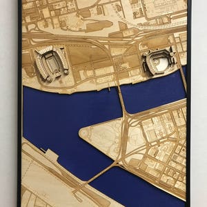 May include: A laser-cut wooden map of a city with two stadiums, one a football stadium and the other a baseball stadium, on a blue background.