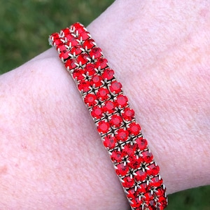 May include: A vintage bracelet with three rows of bright red rhinestones set in a gold-tone metal frame. This classic piece of jewellery is ideal for adding a splash of colour to any outfit.