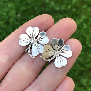 May include: A pair of silver clover earrings with a detailed cut-out design.