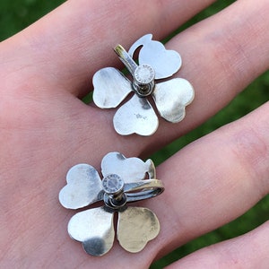 May include: A pair of silver four-leaf clover earrings with a sterling silver stamp on the back.