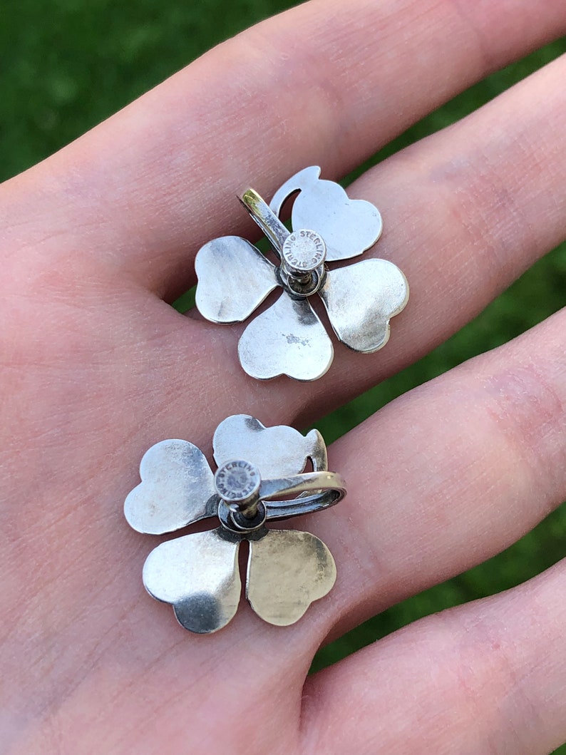 May include: A pair of silver four-leaf clover earrings with a sterling silver stamp on the back.