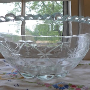 Peut inclure: Un saladier en verre transparent avec un bord festonné et un motif en diamant gravé sur les côtés. Le saladier est posé sur une nappe blanche avec des broderies florales.