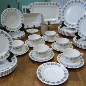 May include: A set of white ceramic dinnerware with a green and brown geometric pattern. The set includes plates, bowls, cups, and saucers.