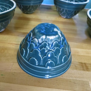 Op de afbeelding: Set van vijf tealblauwe keramische kommen met een gegolfd ontwerp. De kommen zijn allemaal even groot en hebben dezelfde vorm en zijn in een rij op een houten oppervlak gerangschikt.