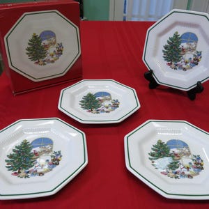 Puede incluir: Juego de cuatro platos de Navidad octogonales blancos con borde verde. Cada plato presenta una ilustración colorida de un árbol de Navidad con regalos y una escena de ventana.