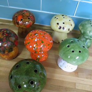 Puede incluir: Siete jarrones de cerámica con forma de hongo en varios colores y patrones. Los jarrones tienen agujeros en la parte superior para flores.