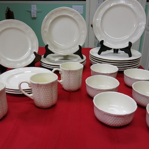 Puede incluir: Un juego de vajilla de cerámica blanca con un patrón en relieve. El juego incluye platos llanos, platos para ensalada, tazones y tazas.