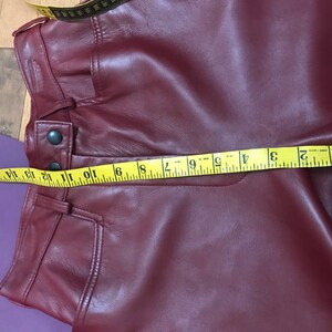 May include: A close-up of a burgundy leather pants with a yellow measuring tape across the waistband. The tape reads 1 to 12 inches.