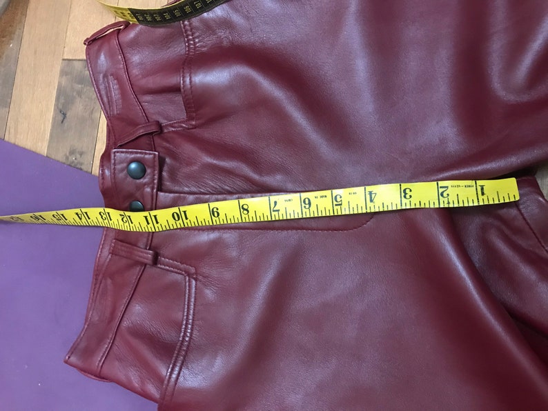 May include: A close-up of a burgundy leather pants with a yellow measuring tape across the waistband. The tape reads 1 to 12 inches.
