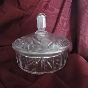 May include: A clear glass candy dish with a cut glass design and a crystal knob lid.